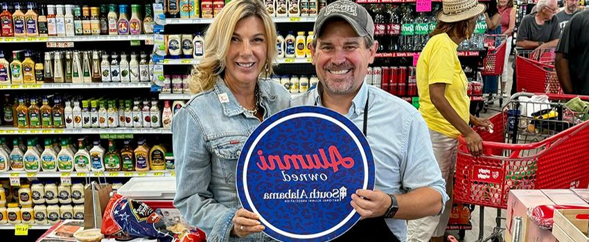 Play House Spices at the grocery store holding up Alumni owned sign.